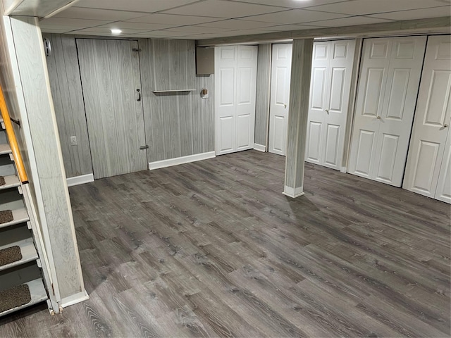 basement featuring a drop ceiling, wooden walls, and dark hardwood / wood-style floors