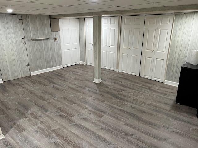 basement with wooden walls, dark hardwood / wood-style flooring, and a drop ceiling