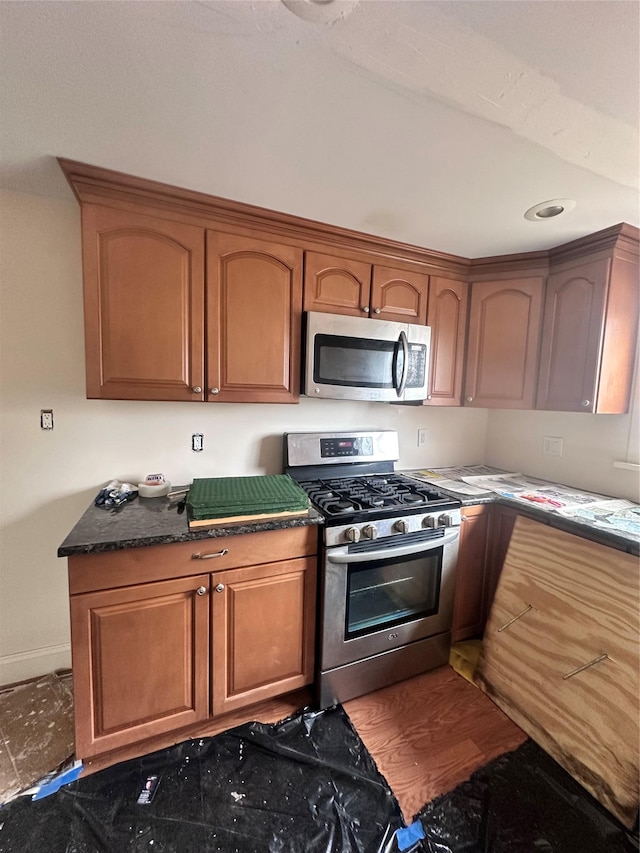 kitchen with hardwood / wood-style flooring, stainless steel appliances, and dark stone countertops