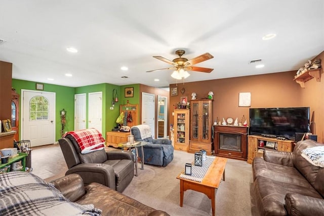 living room with a fireplace, light colored carpet, and ceiling fan