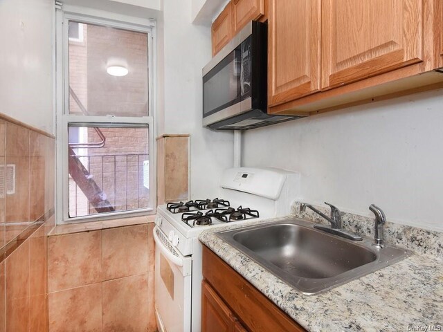 kitchen with light stone countertops, sink, and white range with gas cooktop