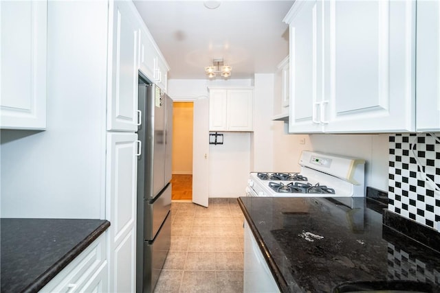 kitchen featuring backsplash, dark stone counters, white gas stove, white cabinetry, and stainless steel refrigerator