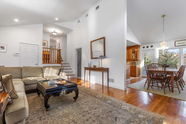 living area featuring high vaulted ceiling, stairs, visible vents, and wood finished floors