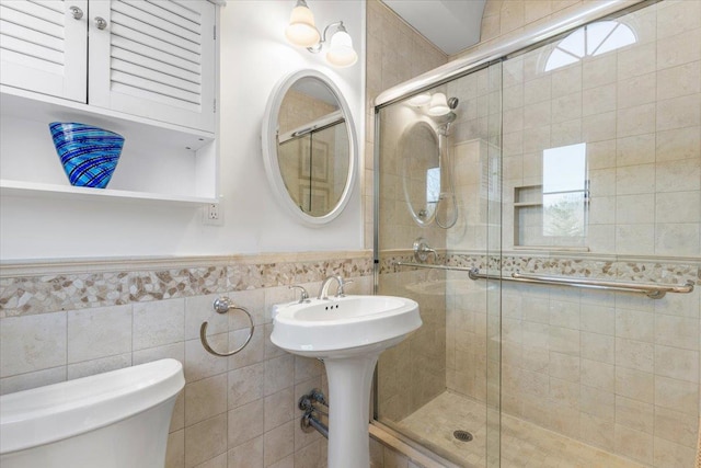 full bath featuring a wainscoted wall, tile walls, toilet, a sink, and a shower stall