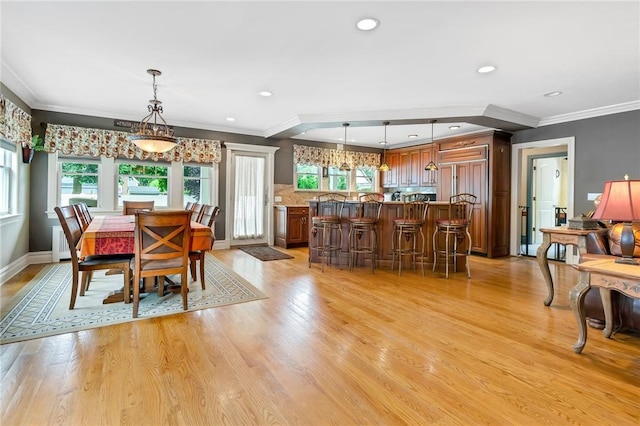 dining area with light wood-type flooring, crown molding, and a healthy amount of sunlight