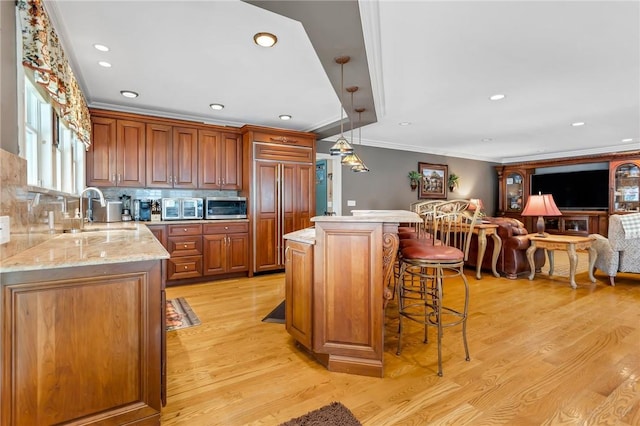 kitchen with a breakfast bar, backsplash, hanging light fixtures, light wood-type flooring, and paneled fridge