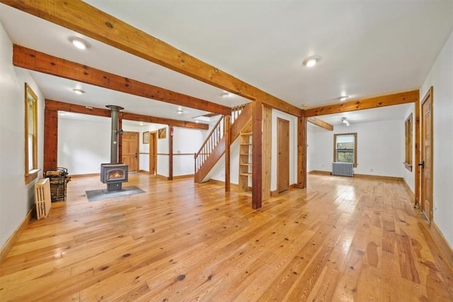 unfurnished living room featuring a wood stove, light hardwood / wood-style flooring, beamed ceiling, and radiator