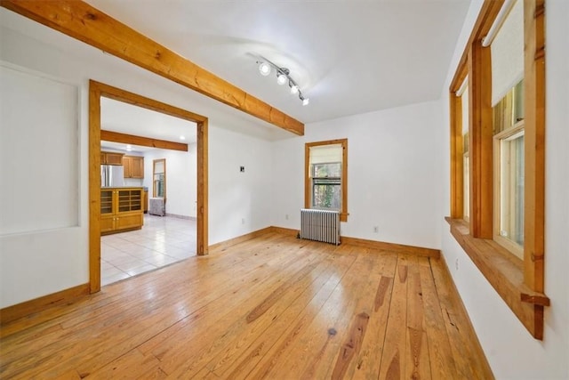 empty room with radiator heating unit, beamed ceiling, track lighting, and light wood-type flooring