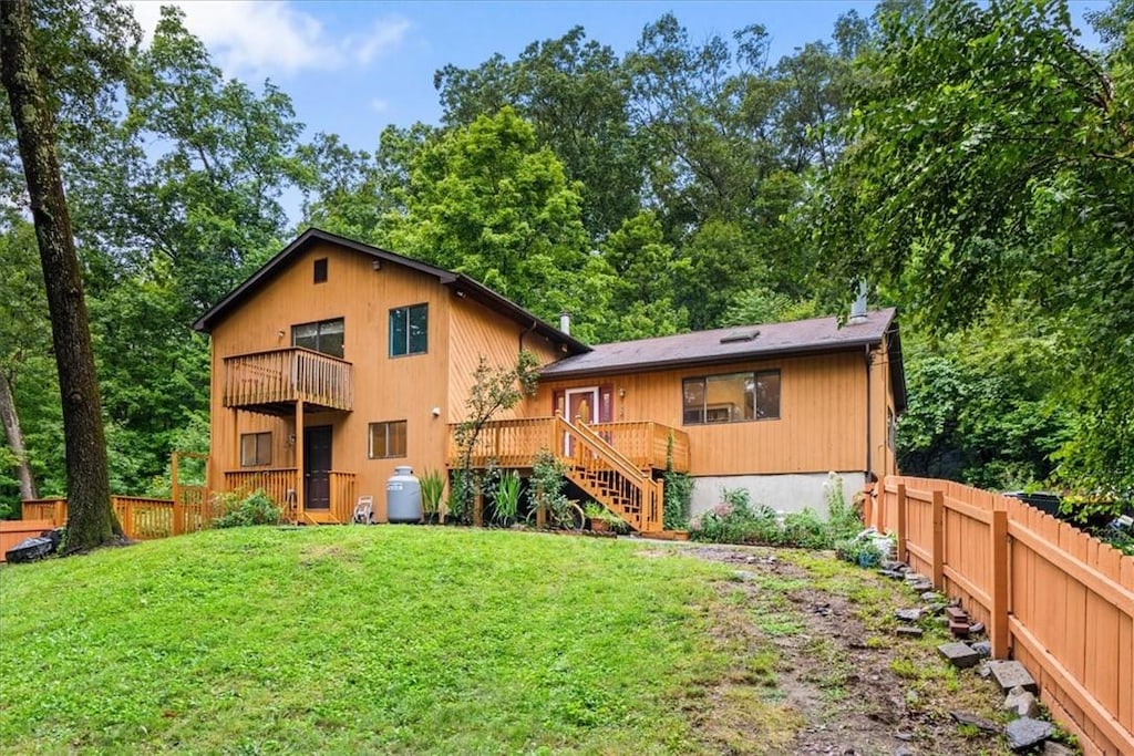 rear view of house with a balcony, a wooden deck, and a lawn