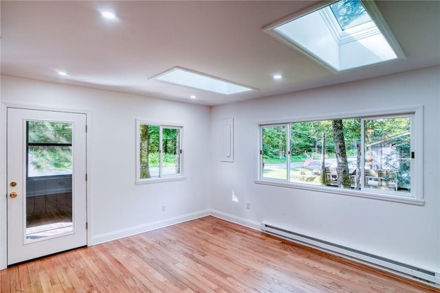 empty room with a skylight, light wood-type flooring, and a baseboard heating unit