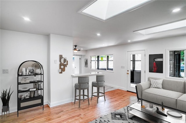 living room with a skylight, ceiling fan, and light hardwood / wood-style floors