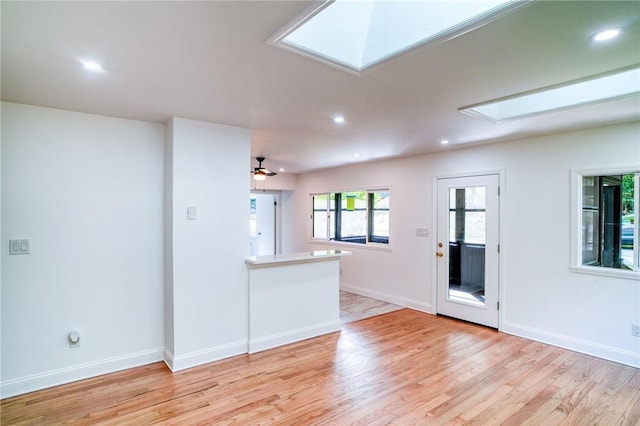 unfurnished living room with ceiling fan, light wood-type flooring, and a skylight