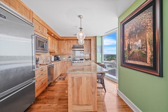 kitchen featuring decorative backsplash, light wood-type flooring, built in appliances, a center island, and hanging light fixtures