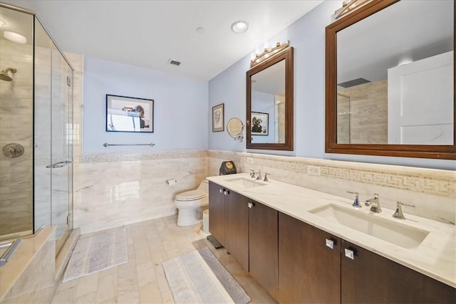 bathroom with vanity, toilet, a shower with door, and tile walls