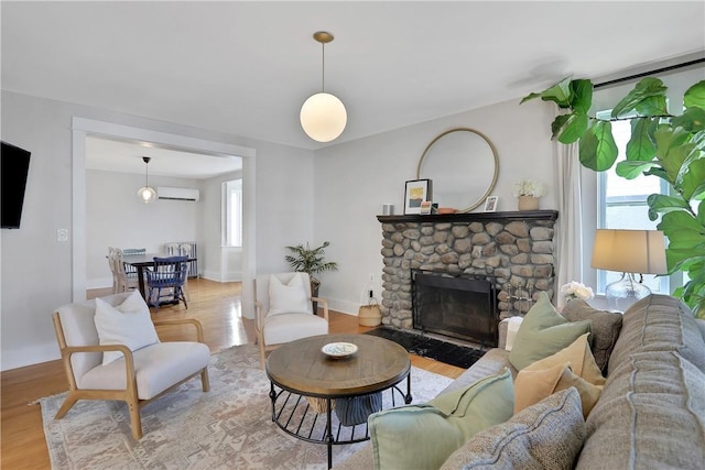 living room featuring a wall mounted air conditioner, light hardwood / wood-style floors, and a stone fireplace