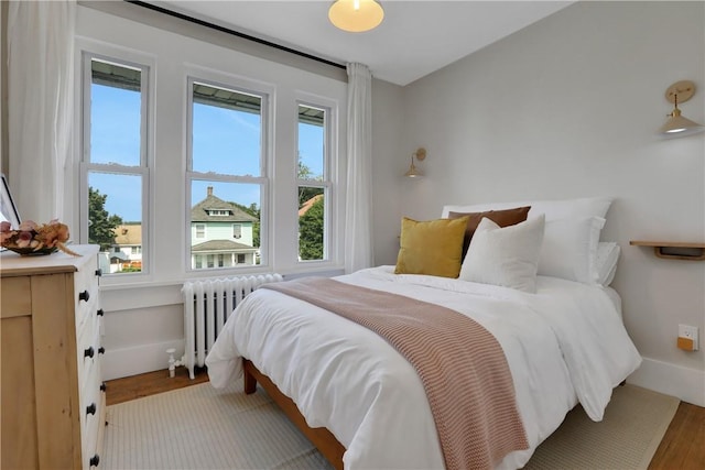 bedroom with hardwood / wood-style floors, radiator, and multiple windows