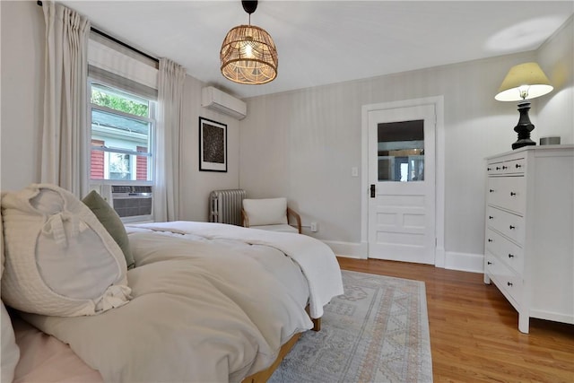 bedroom with radiator heating unit, light wood-type flooring, a wall mounted AC, and cooling unit