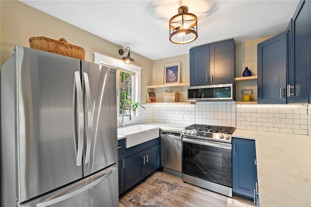 kitchen with sink, light wood-type flooring, blue cabinetry, light stone countertops, and appliances with stainless steel finishes