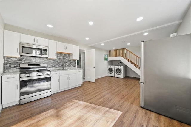 kitchen featuring washing machine and dryer, appliances with stainless steel finishes, decorative backsplash, white cabinets, and light wood-type flooring