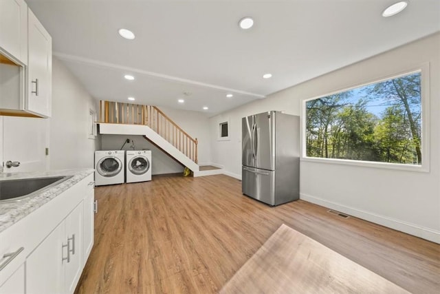 kitchen with white cabinets, sink, stainless steel fridge, light wood-type flooring, and washing machine and clothes dryer