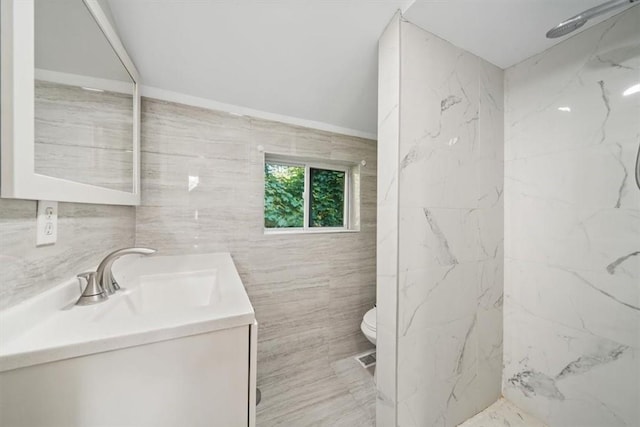 bathroom with vanity, toilet, tiled shower, and tile walls