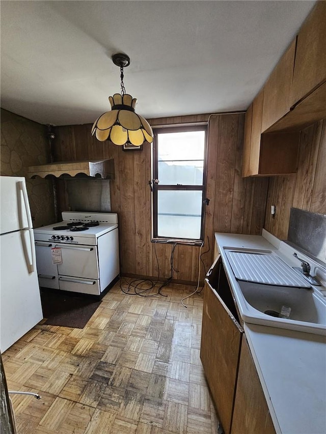 kitchen with sink, pendant lighting, white appliances, wooden walls, and light parquet flooring