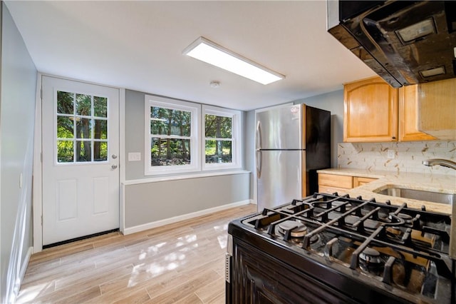 kitchen with stove, backsplash, sink, light hardwood / wood-style floors, and stainless steel refrigerator