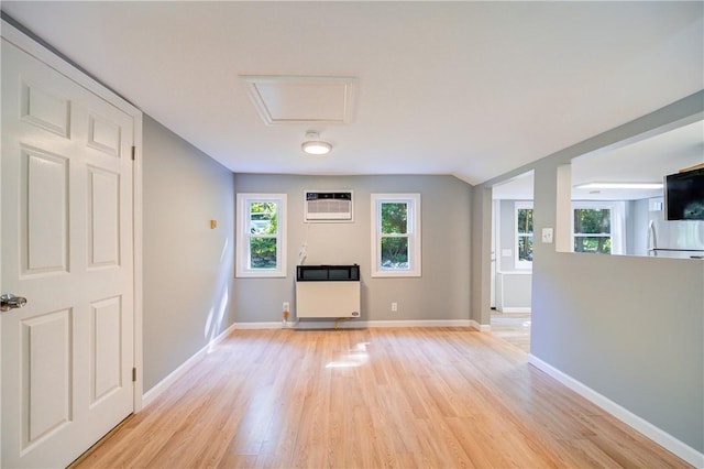 unfurnished living room featuring a wall unit AC, heating unit, a healthy amount of sunlight, and light wood-type flooring