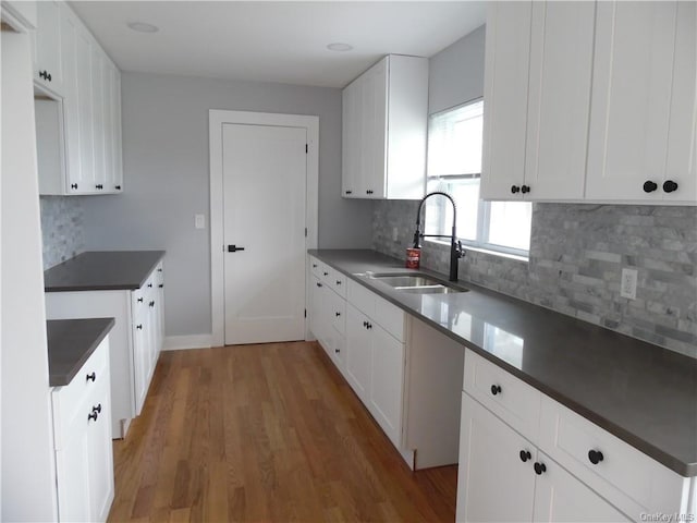 kitchen with hardwood / wood-style floors, backsplash, white cabinetry, and sink