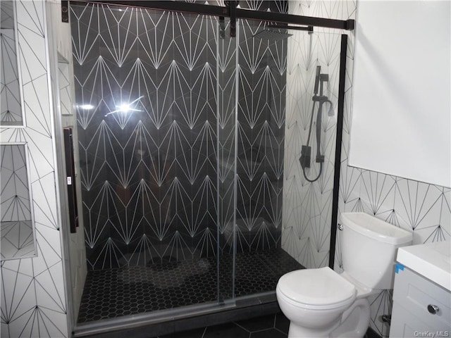 bathroom with vanity, a shower with shower door, tile walls, and toilet