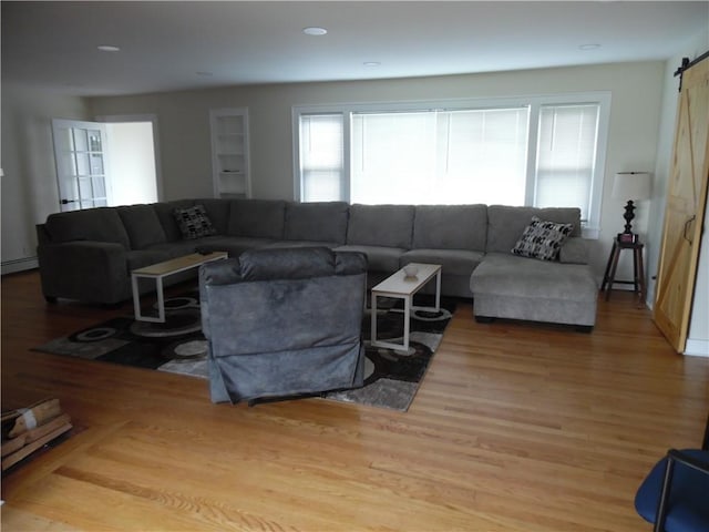 living room with wood-type flooring, a barn door, and a baseboard radiator