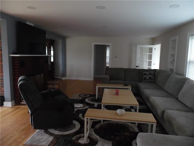 living room with a brick fireplace, built in features, and light hardwood / wood-style flooring