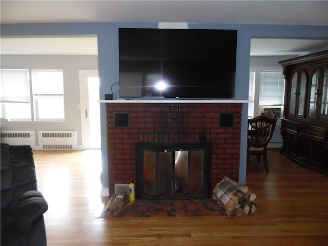 living room featuring wood-type flooring, baseboard heating, radiator, and a brick fireplace