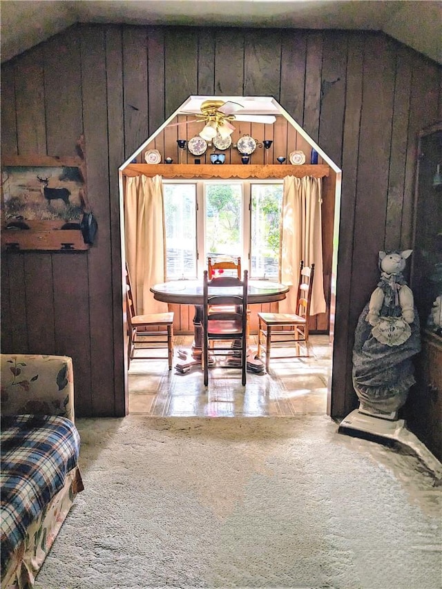 dining space featuring ceiling fan, wooden walls, and vaulted ceiling