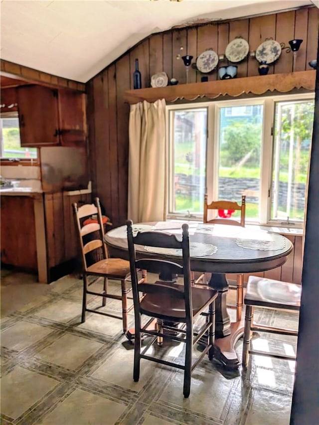 dining room with vaulted ceiling, a wealth of natural light, and wood walls