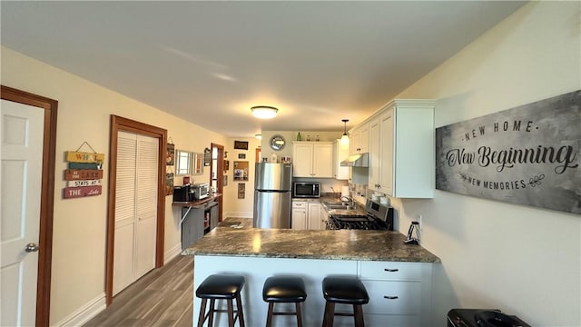 kitchen featuring kitchen peninsula, stainless steel appliances, dark wood-type flooring, white cabinetry, and a breakfast bar area