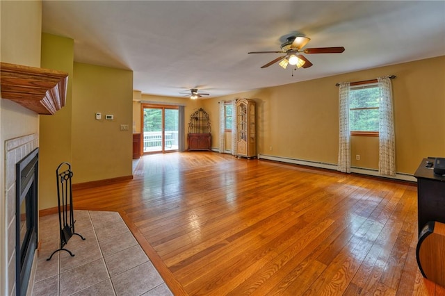 living room with ceiling fan, baseboard heating, a tile fireplace, and light hardwood / wood-style flooring