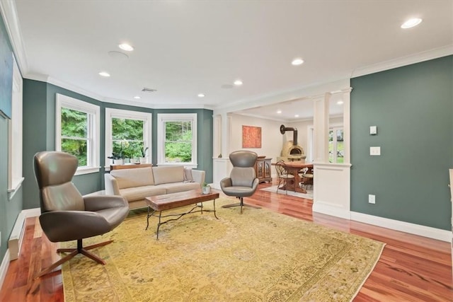 living room featuring ornate columns, light wood-type flooring, crown molding, and a wood stove