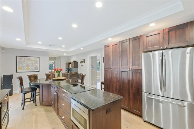 kitchen featuring a tray ceiling, light hardwood / wood-style flooring, a kitchen island, and stainless steel appliances