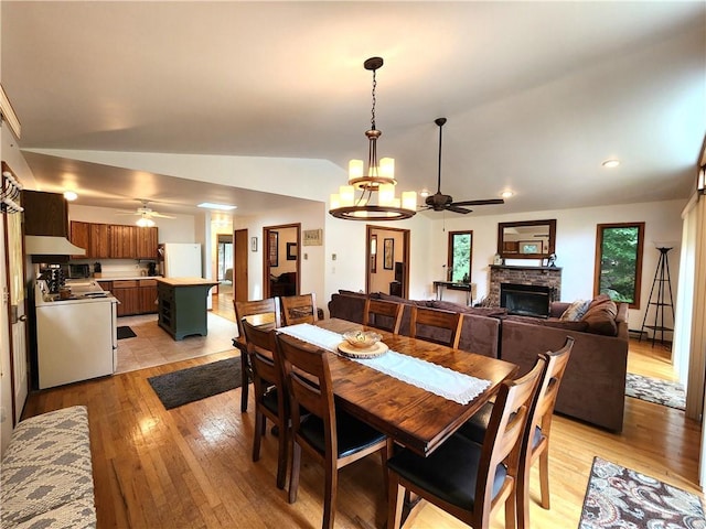 dining space with a fireplace, light wood-type flooring, ceiling fan with notable chandelier, and lofted ceiling