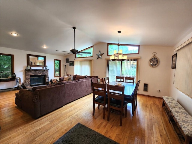 dining space with ceiling fan with notable chandelier, light hardwood / wood-style floors, vaulted ceiling, and a brick fireplace