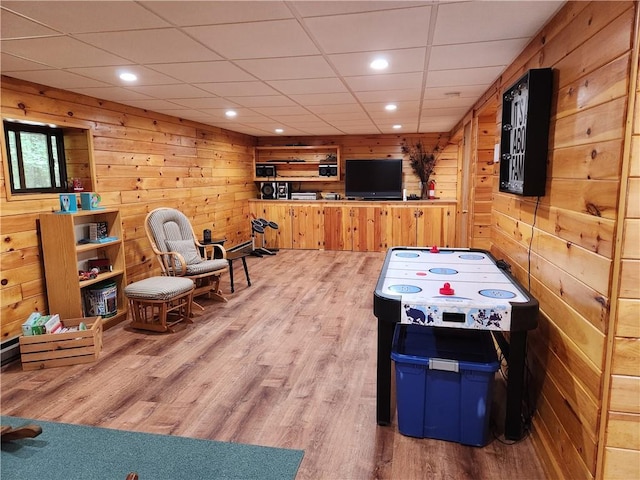 rec room with a paneled ceiling, light hardwood / wood-style floors, and wood walls