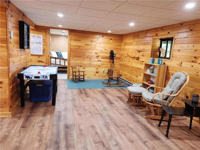 recreation room with wooden walls, light hardwood / wood-style flooring, and a drop ceiling