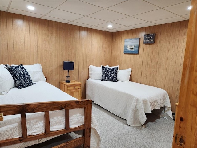 carpeted bedroom with a paneled ceiling and wood walls