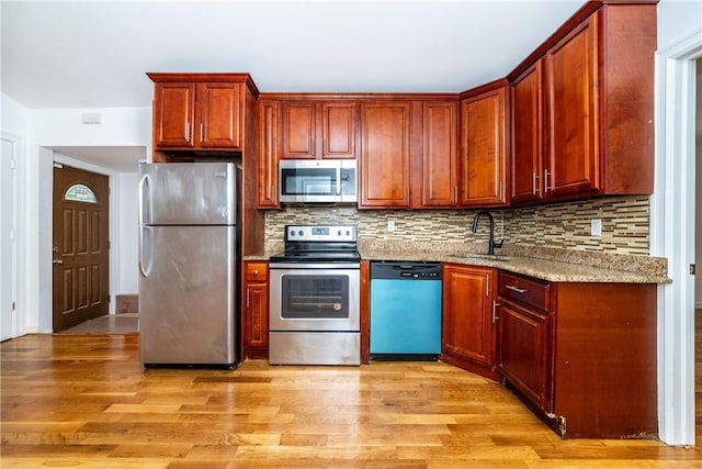 kitchen with backsplash, sink, light hardwood / wood-style flooring, light stone counters, and stainless steel appliances