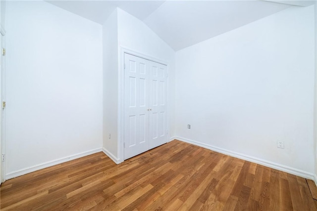 spare room featuring wood-type flooring and vaulted ceiling