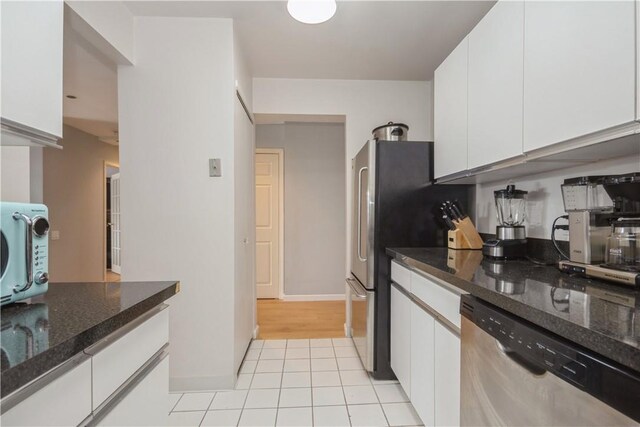 kitchen with light tile patterned flooring, baseboards, white cabinets, stainless steel dishwasher, and dark stone countertops