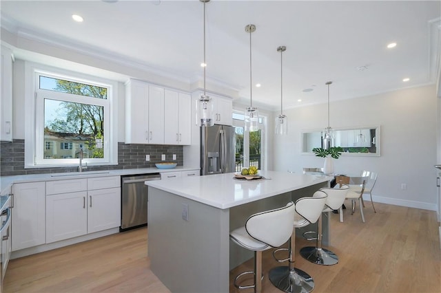 kitchen featuring white cabinets, sink, appliances with stainless steel finishes, decorative light fixtures, and a kitchen island