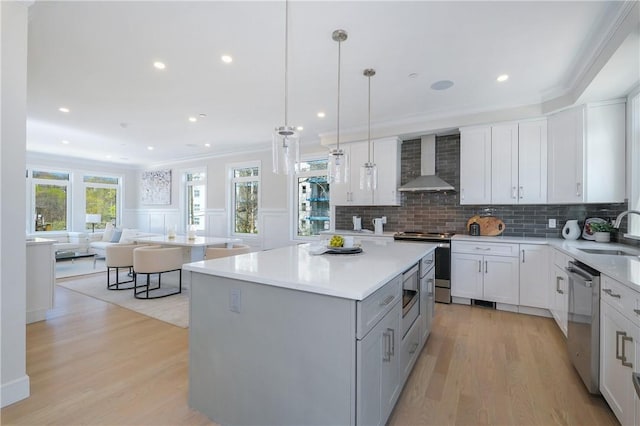 kitchen with appliances with stainless steel finishes, wall chimney range hood, light hardwood / wood-style flooring, white cabinets, and a center island