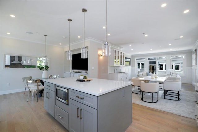 kitchen featuring pendant lighting, light wood-type flooring, stainless steel microwave, and gray cabinetry